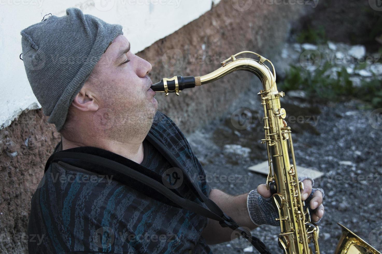 un músico callejero sin hogar se sienta en la calle con un saxofón para ganarse la comida. foto