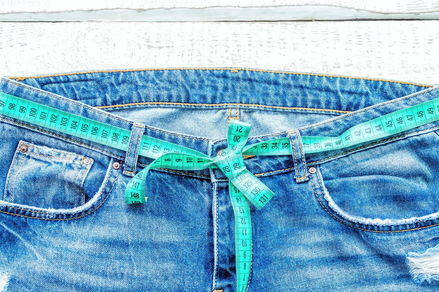 Top of denim trousers, on a wooden background. Blue jeans with a measuring tape instead of a belt. jeans with a measuring tape around the waist. The concept of a healthy lifestyle and diet. photo