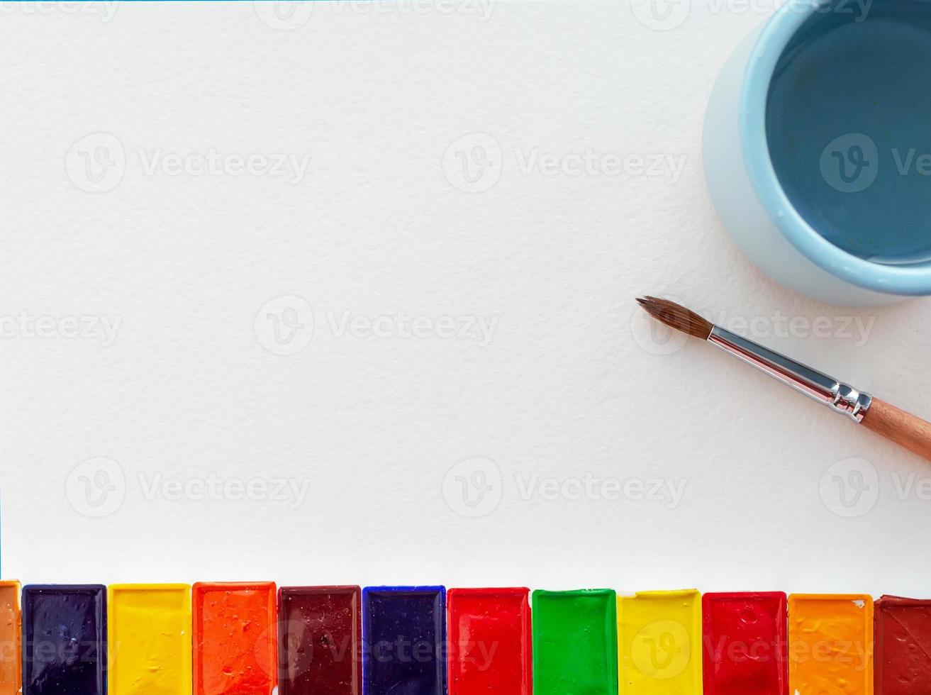 Watercolor paints, a sakan with water, a brush and a white sheet on the artist's table. Close-up. photo