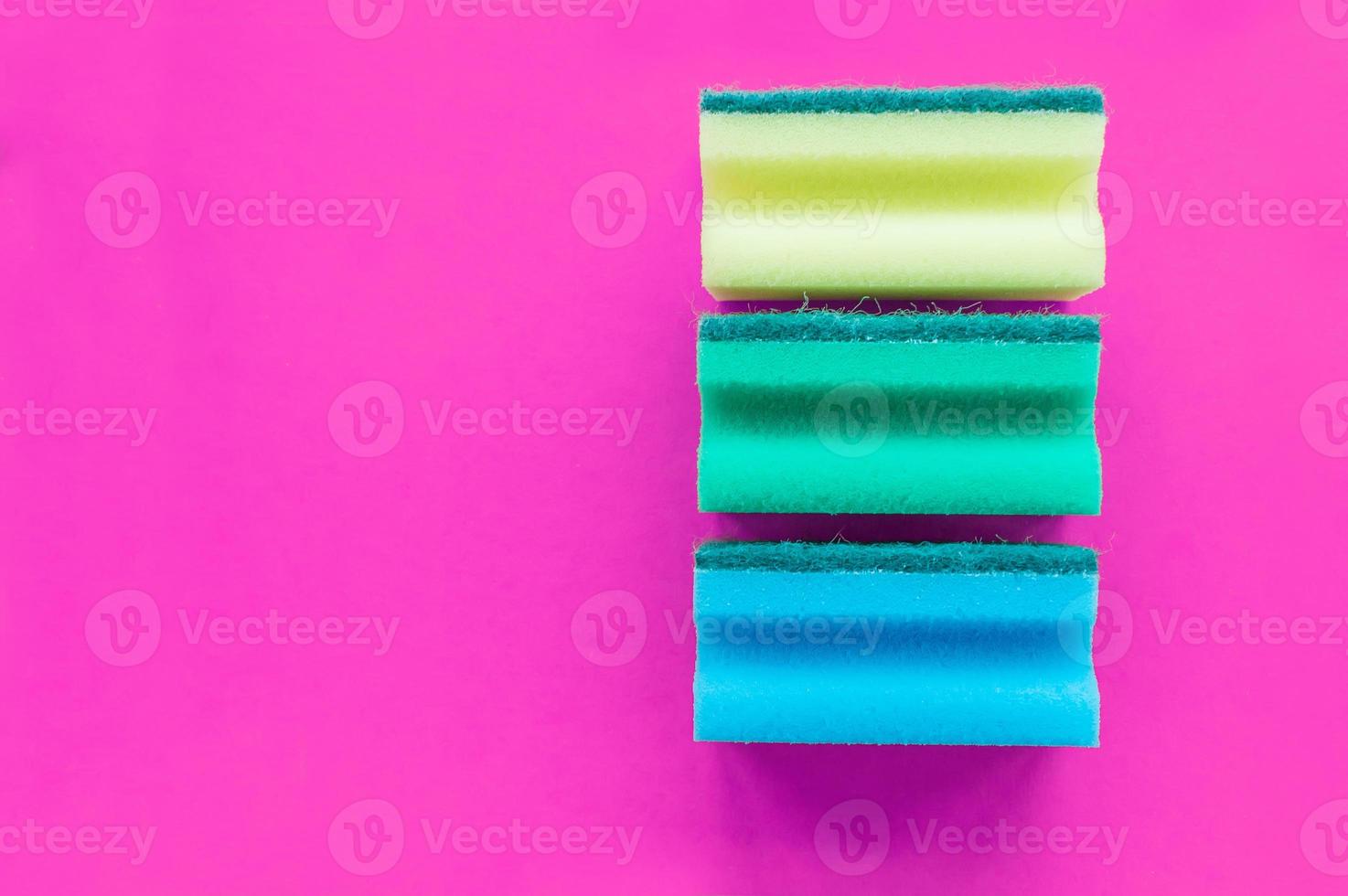 A stack of multicolored dishwashing sponges on a pink background with space for writing. photo