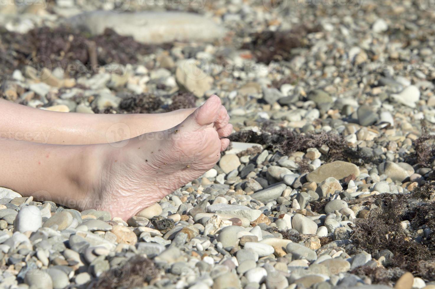 The girl's legs are wrinkled from the water on a pebble beach in the sun. The concept of tourism. photo