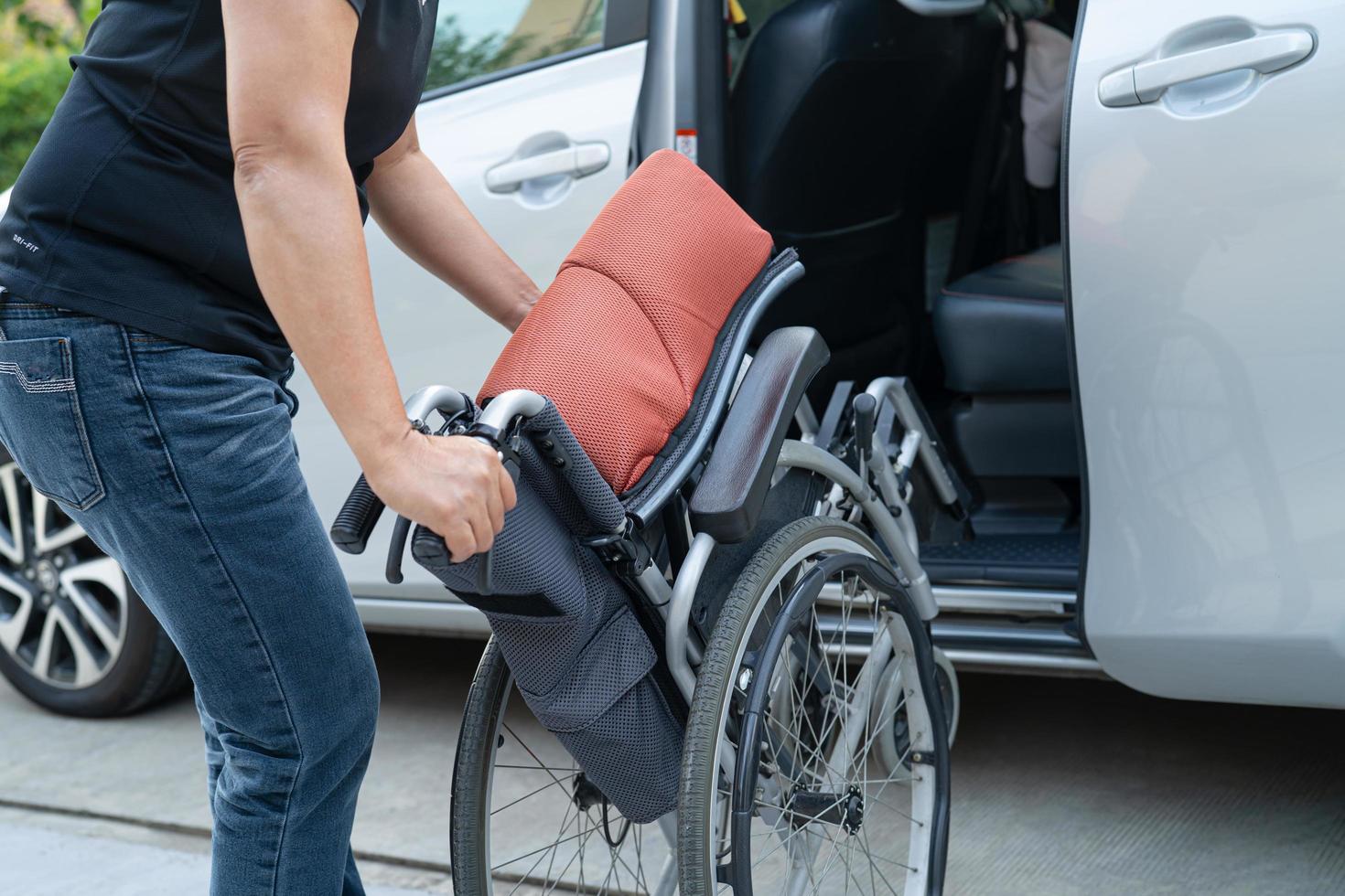 Asian woman folding and lift up wheelchair into her car. Accessibility concept. photo