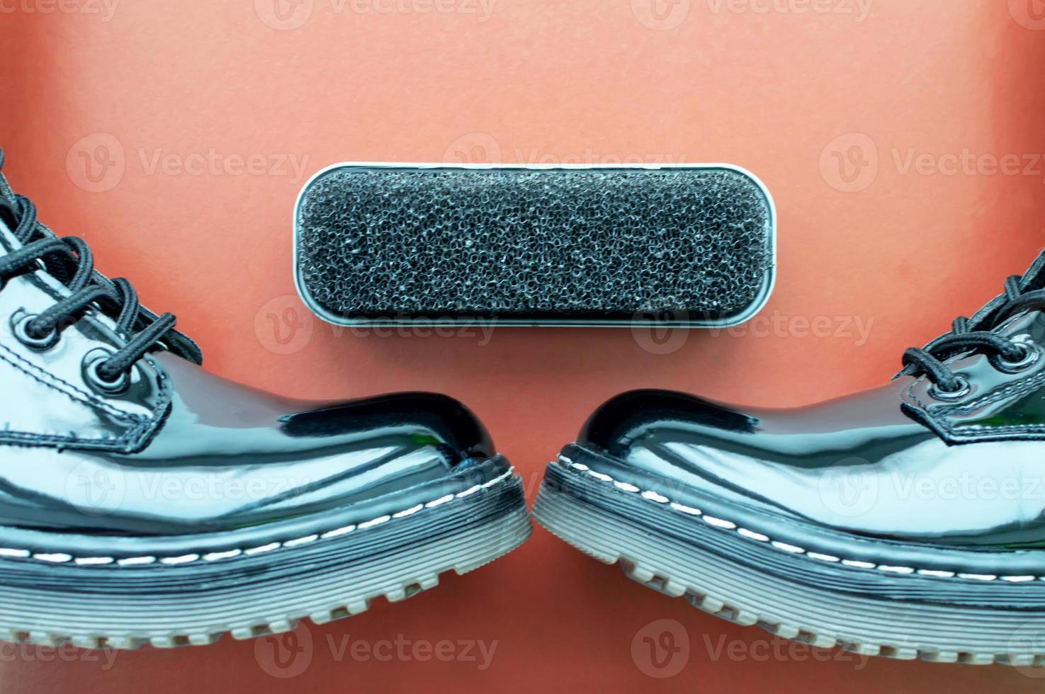 una esponja para zapatos junto a unos zapatos de charol negro pulido sobre un fondo naranja. de cerca. foto