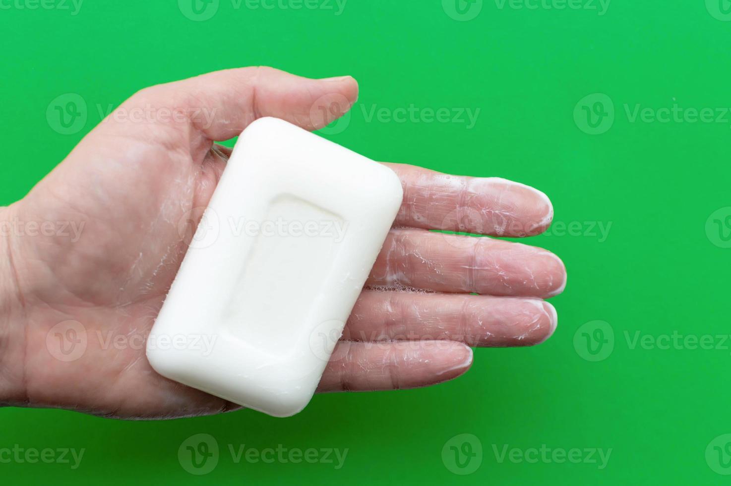 White soap in a man's hand on a green background. Concept of hygiene and body care. photo