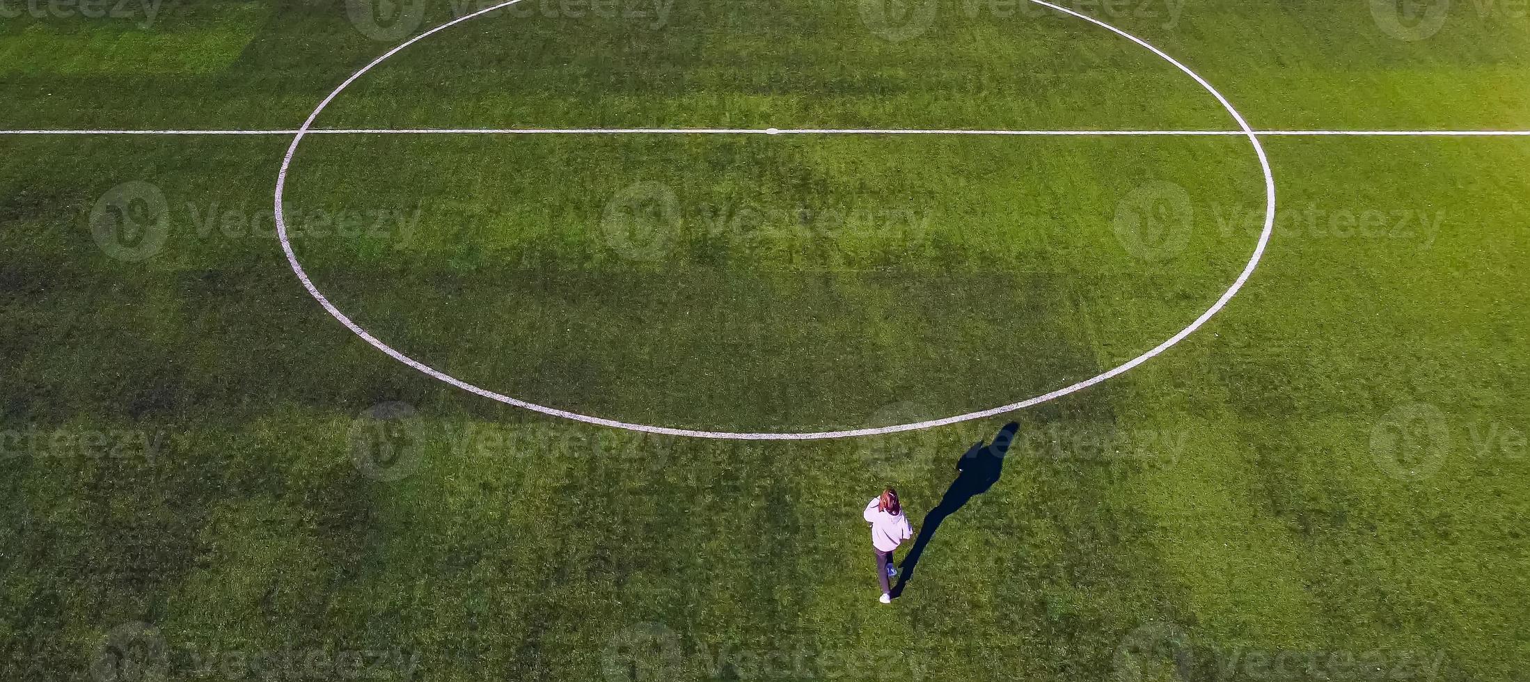 una pequeña adolescente corre rápidamente por el campo de fútbol del estadio para luchar por la victoria disparando desde una vista de pájaro por un dron foto