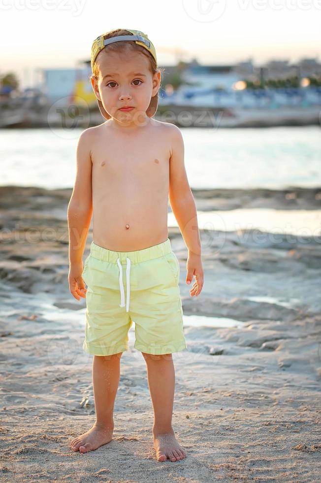 A boy in shorts and a cap on the beach on a Sunny day. Tourism, travel, family vacations. photo