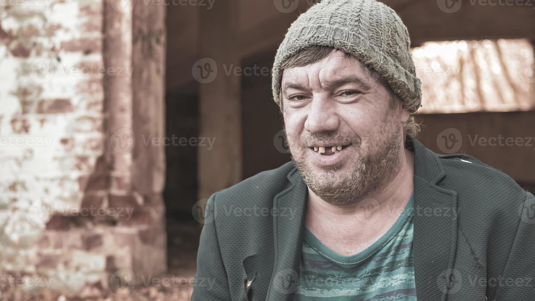 a poor homeless man in a hat and suit smiles looking at the camera in modern society , the concept of the problem of inequality and pain photo