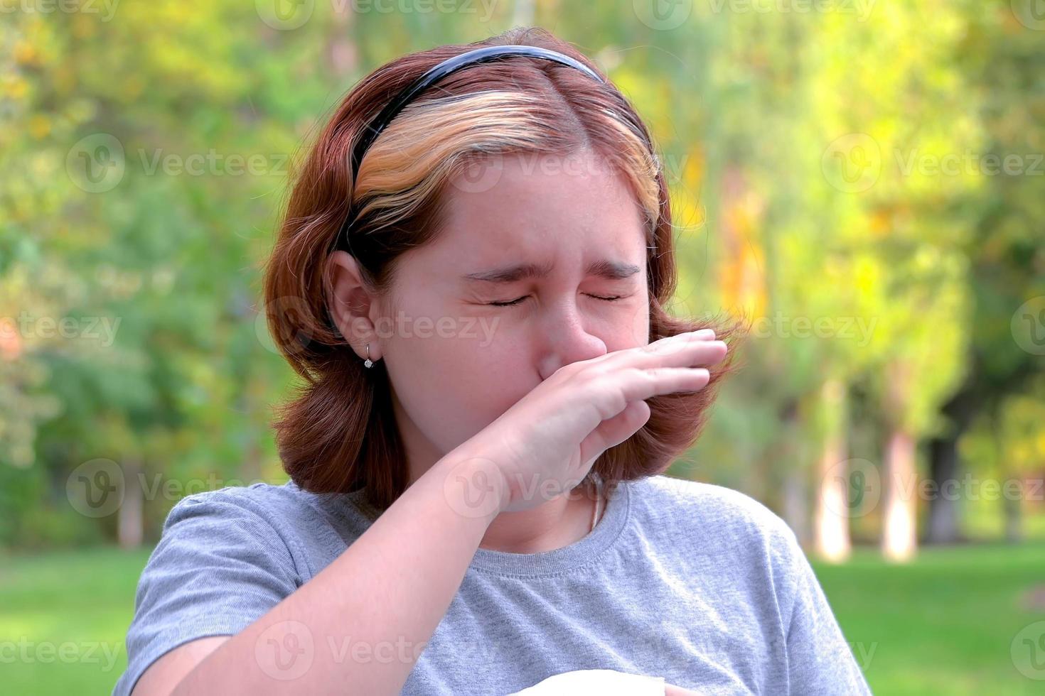 una niña con alergias en un parque de otoño. niña estornuda se limpia la nariz con la mano foto