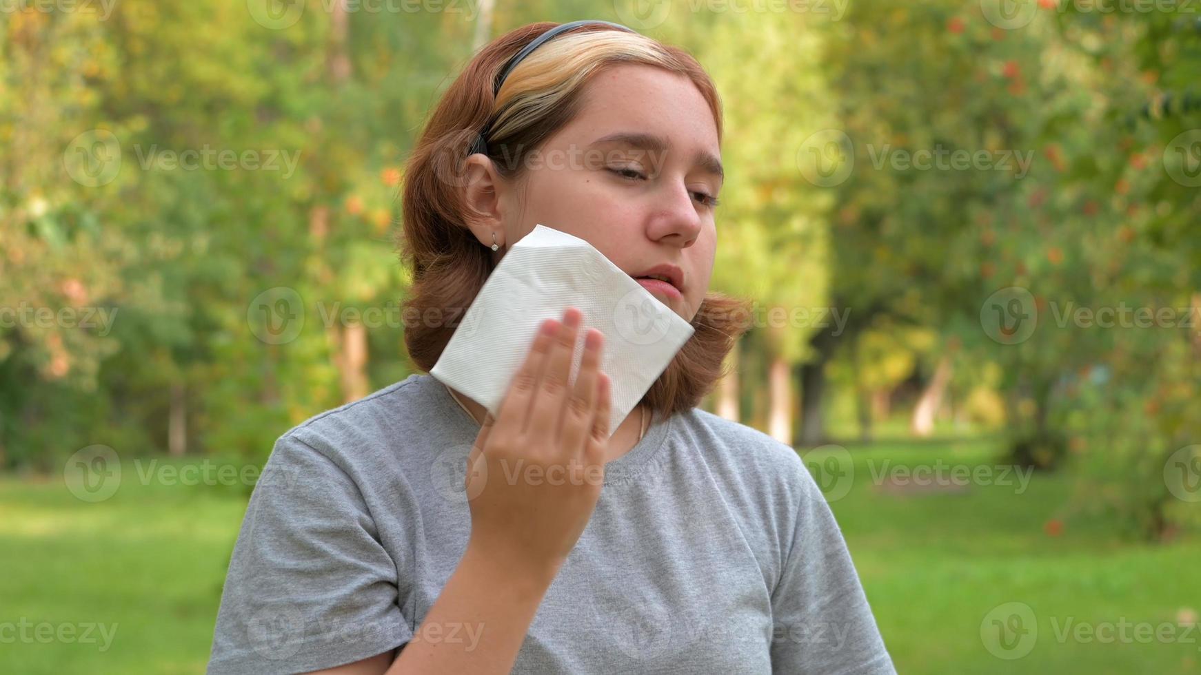 una adolescente con un corte de pelo corto se limpia la cara con una servilleta del sudor en el calor después de comer se limpia los labios foto