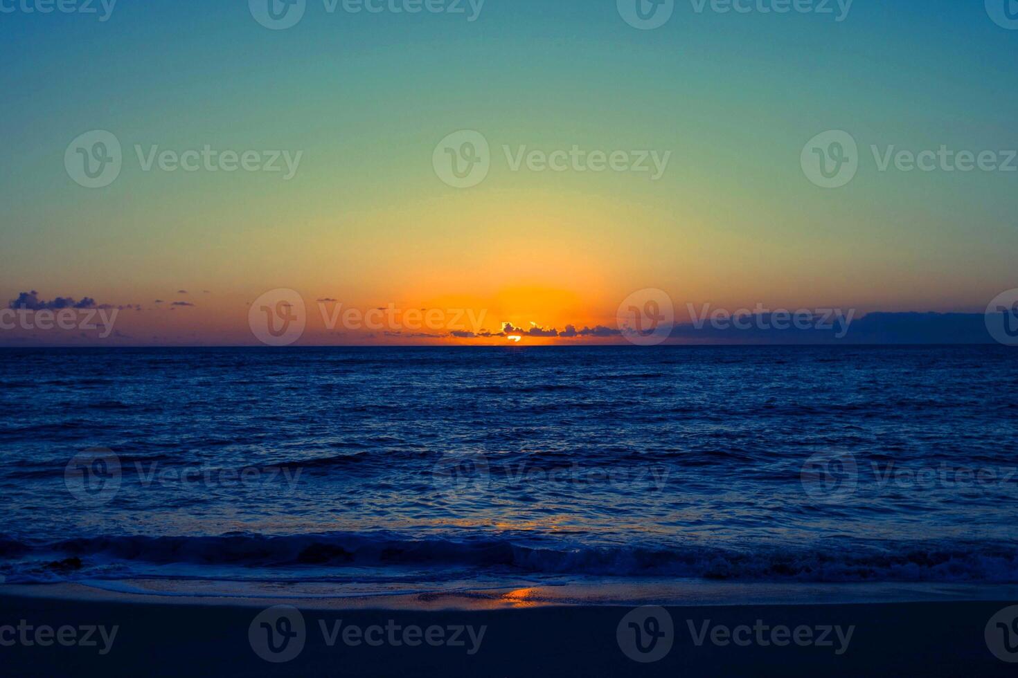 sunset orange in sea and sky blue beautiful sea and sunset with large yellow sun under the sea surface hills in the background. photo