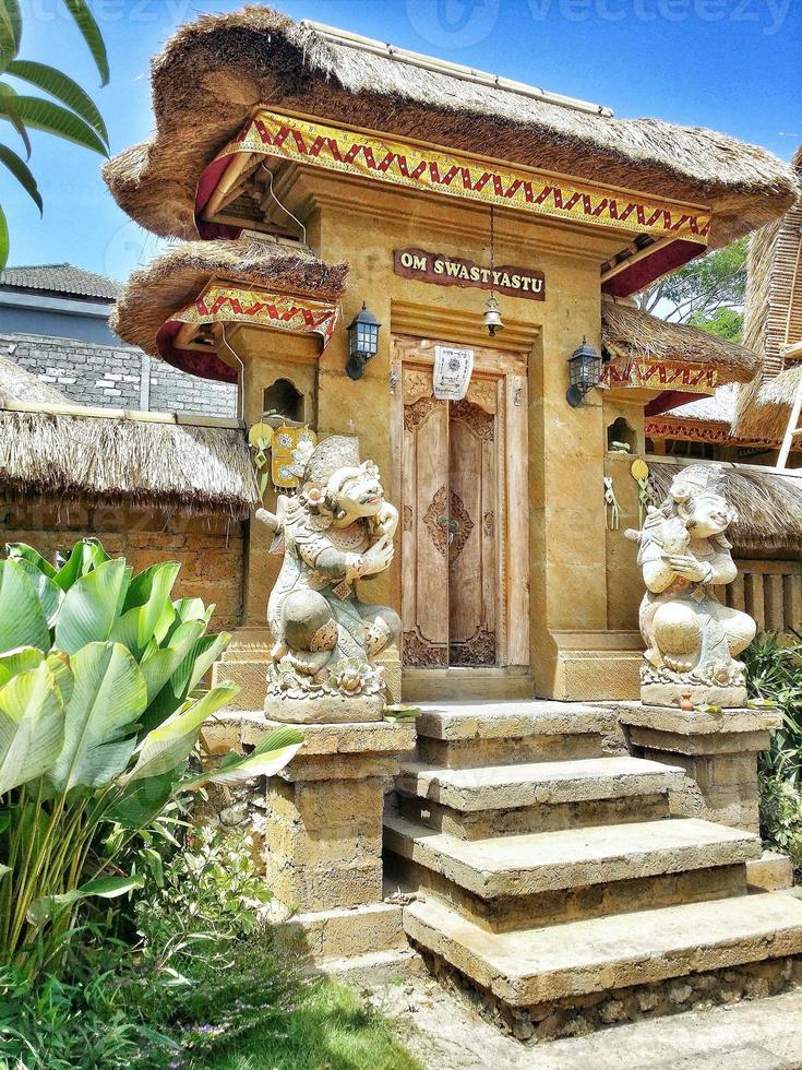 Balinese traditional building in the form of an entrance made of wood with a background of blue sky and green photo