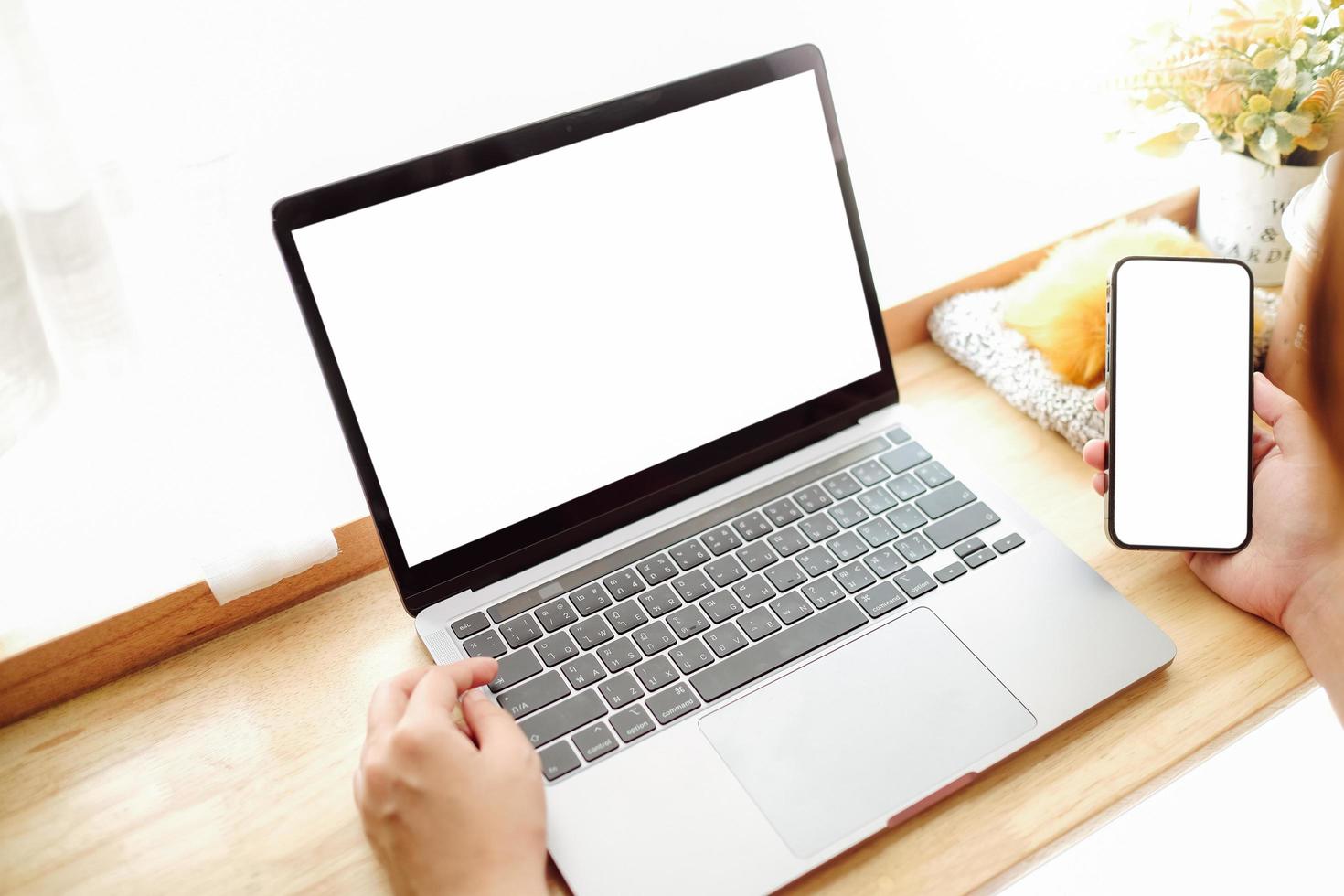 Imagen de maqueta de manos de mujer sosteniendo un teléfono móvil blanco y una computadora portátil con pantalla en blanco en el muslo y una taza de café en el café foto