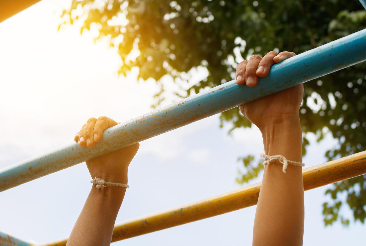 Little boy hanging bar by 2 hands the outdoor exercise equipment in public park, soft focus photo