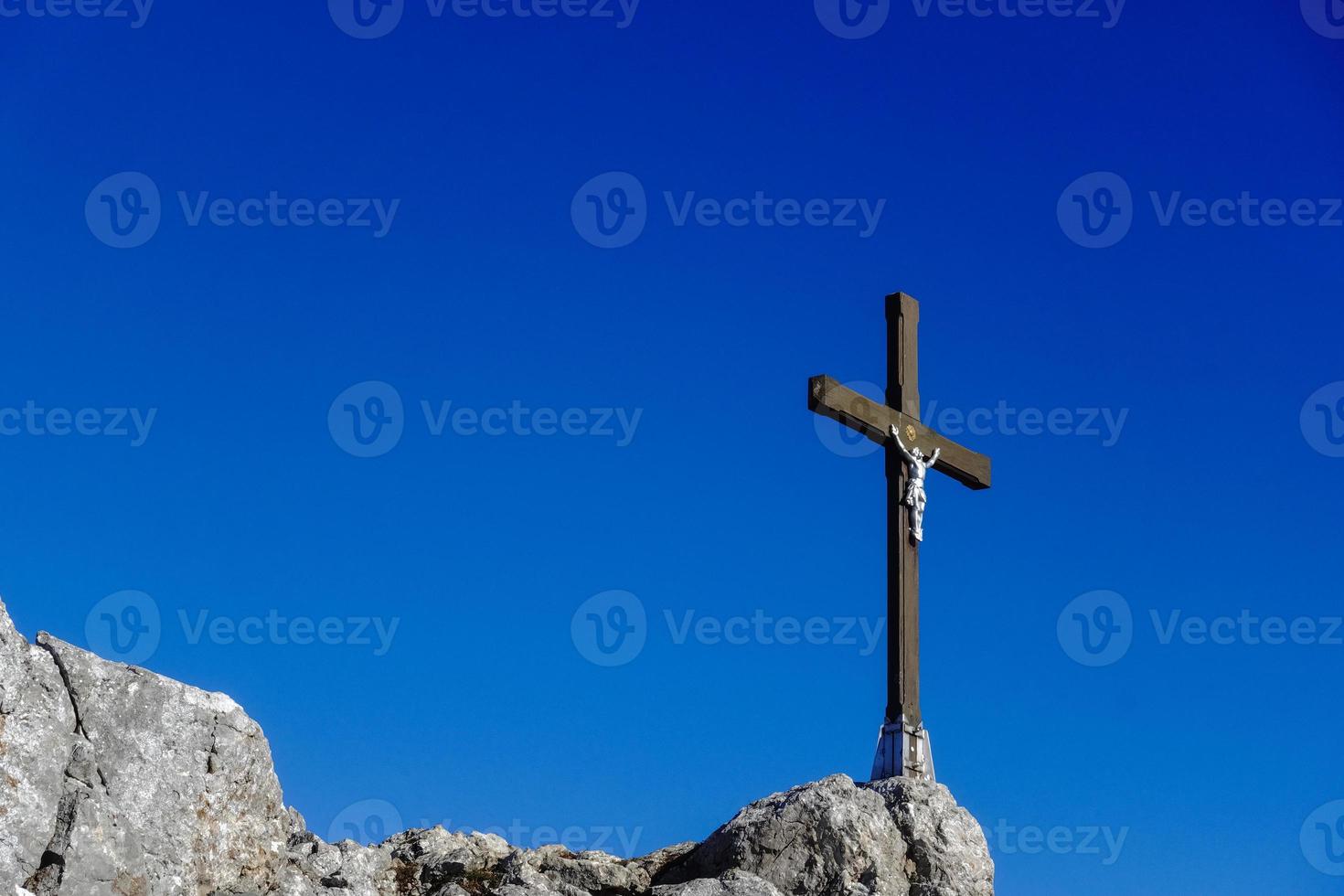 wooden cross with white jesus statue on the rocks at the summit with dark blue sky photo