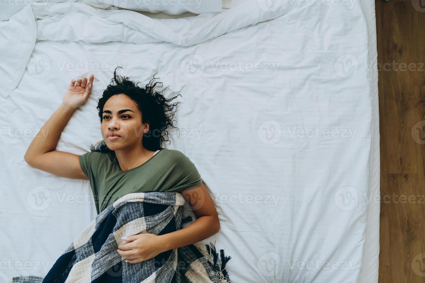 Overhead view of tired African woman in a blanket on the bed photo