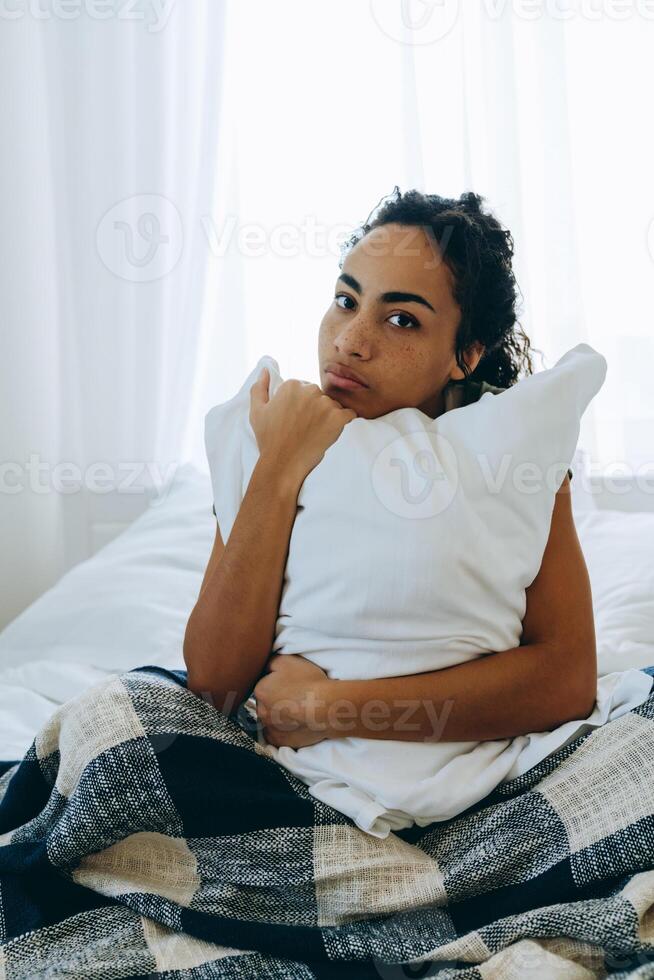 Bored African woman wrapped in a blanket and hugging pillow photo