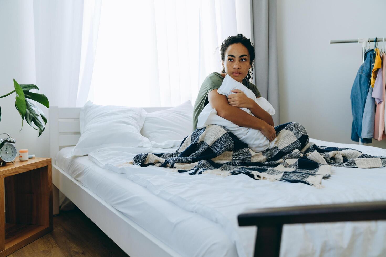 Sad African woman wrapped in a blanket and hugging pillow on her bed at home photo