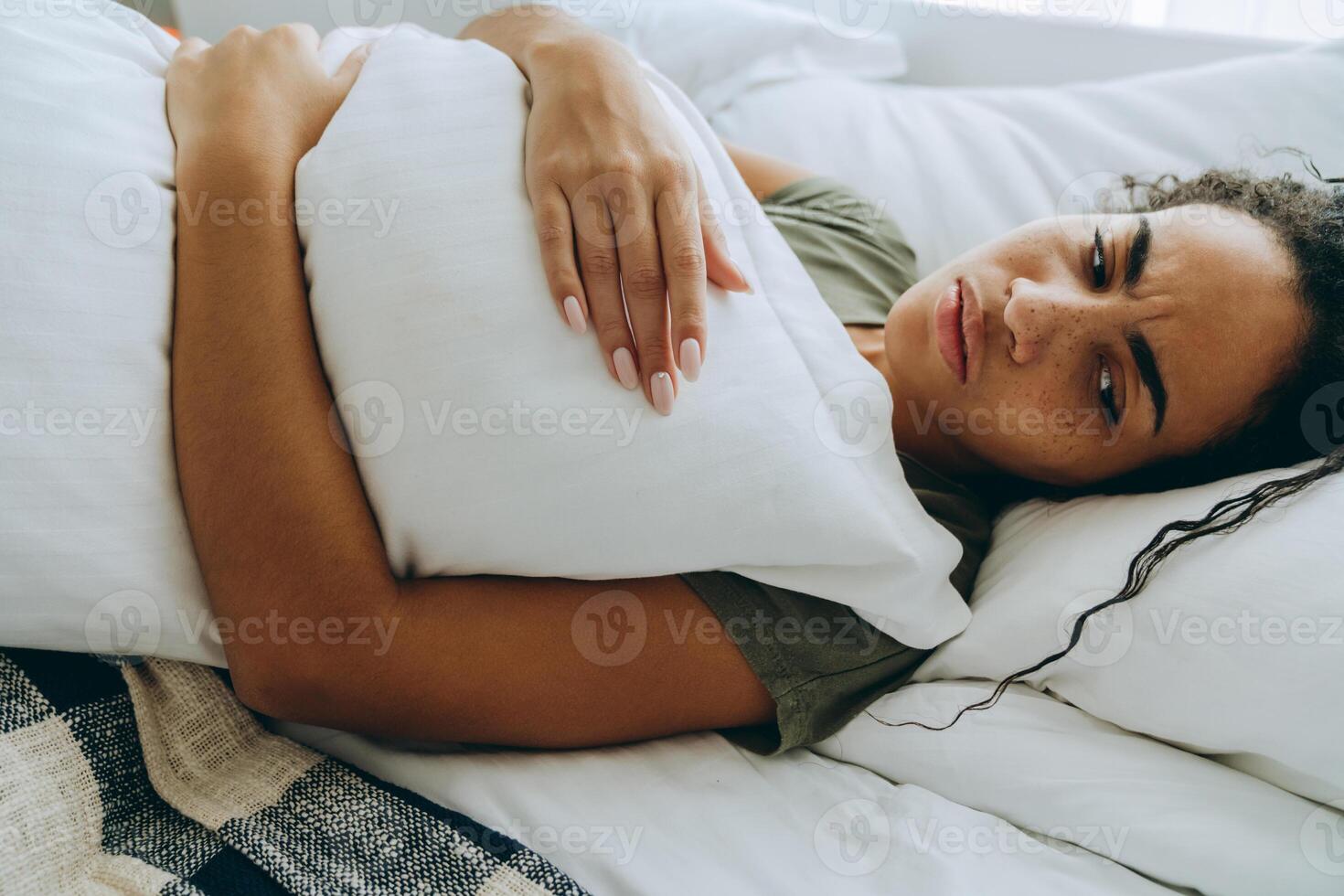Side view of displeased African woman wrapped herself in a blanket and hugging pillow photo