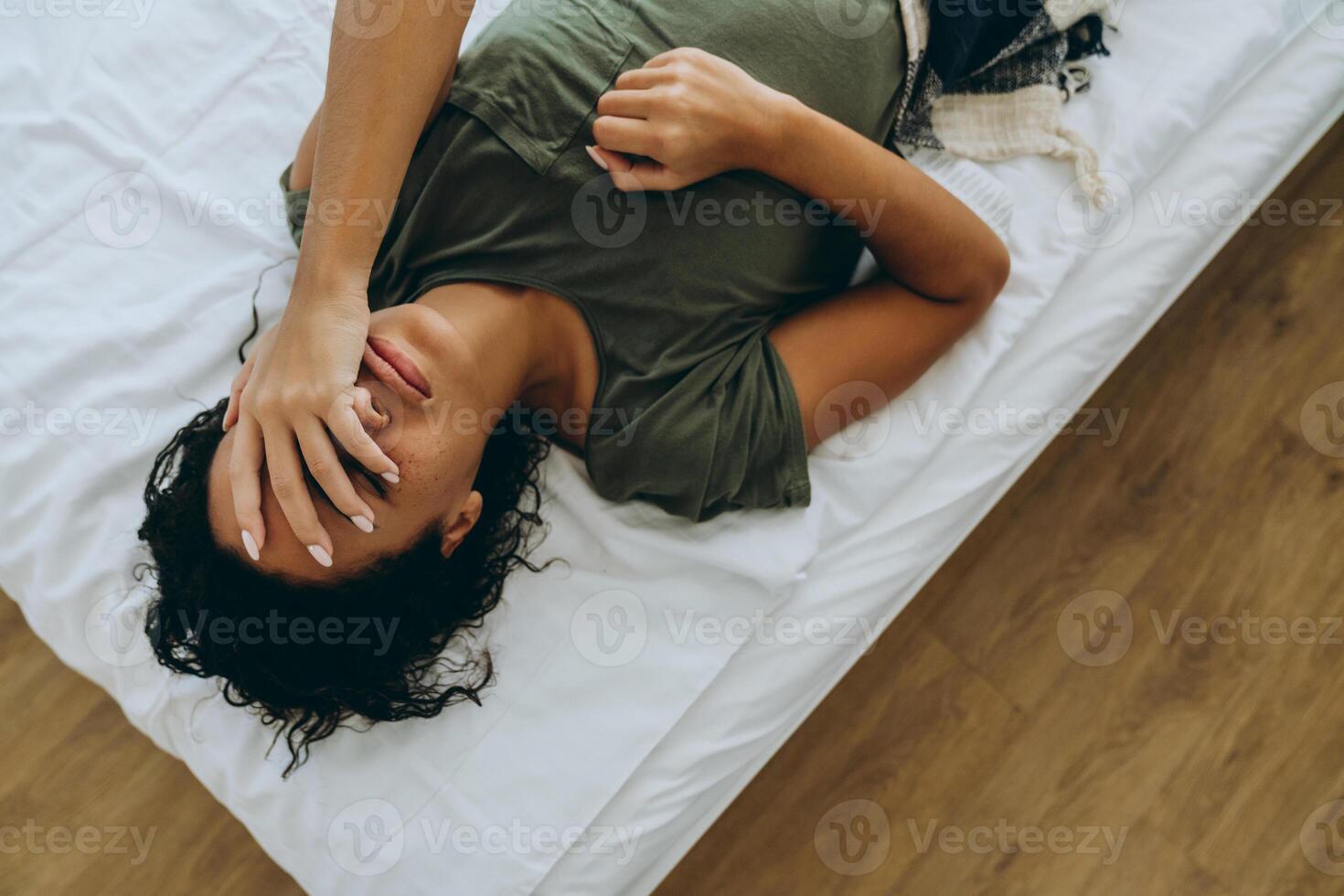 Vista aérea de la mujer triste africana que cubre su rostro con la mano en la cama foto
