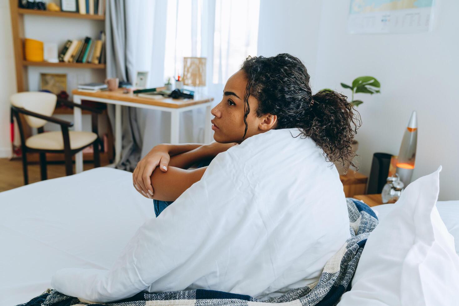 Vista lateral de la mujer afroamericana pensativa envuelta en una manta en la cama foto