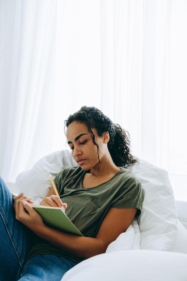Concentrated African woman writing something in notepad on the bed photo