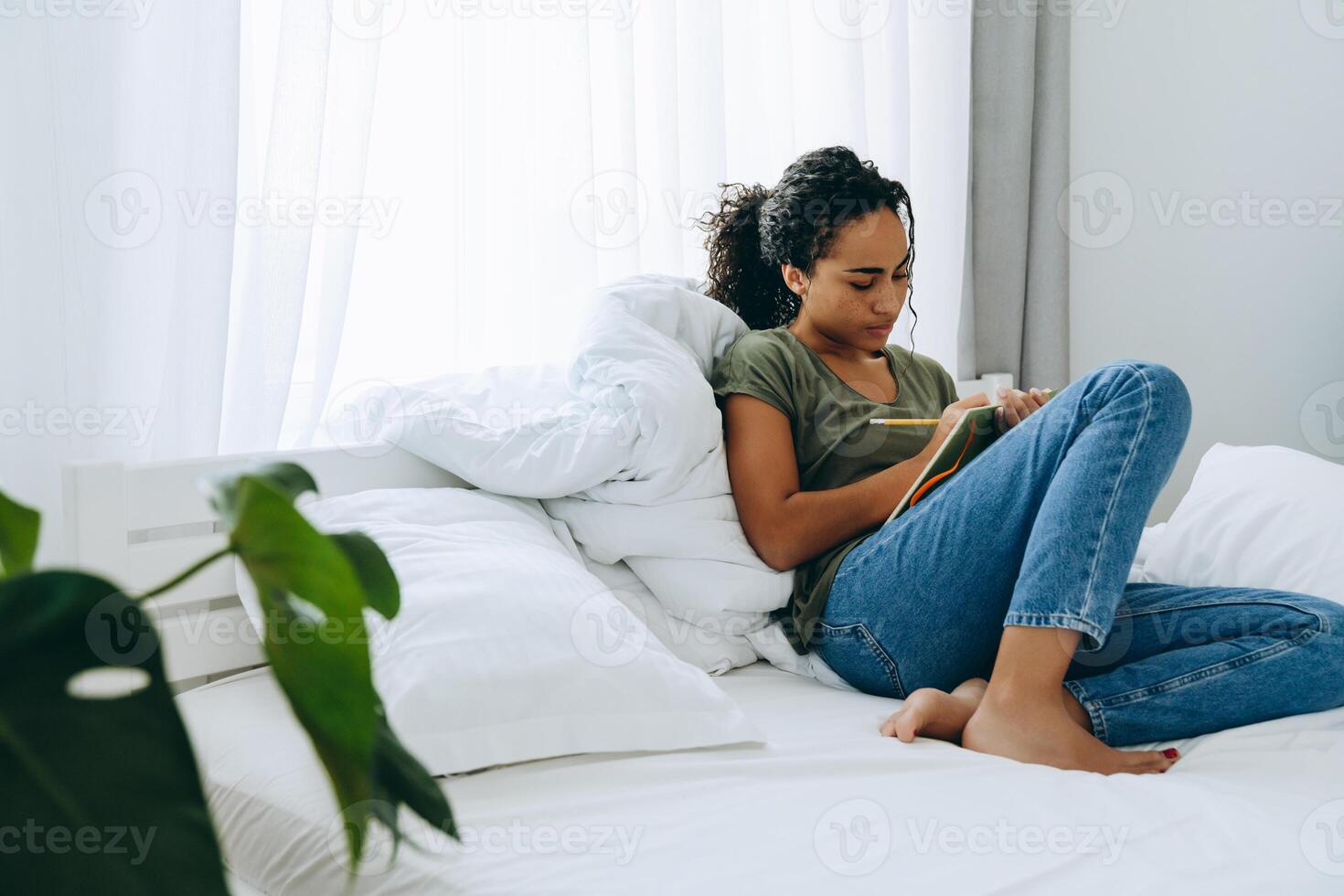 Segura mujer africana escribiendo algo en el bloc de notas en la cama foto