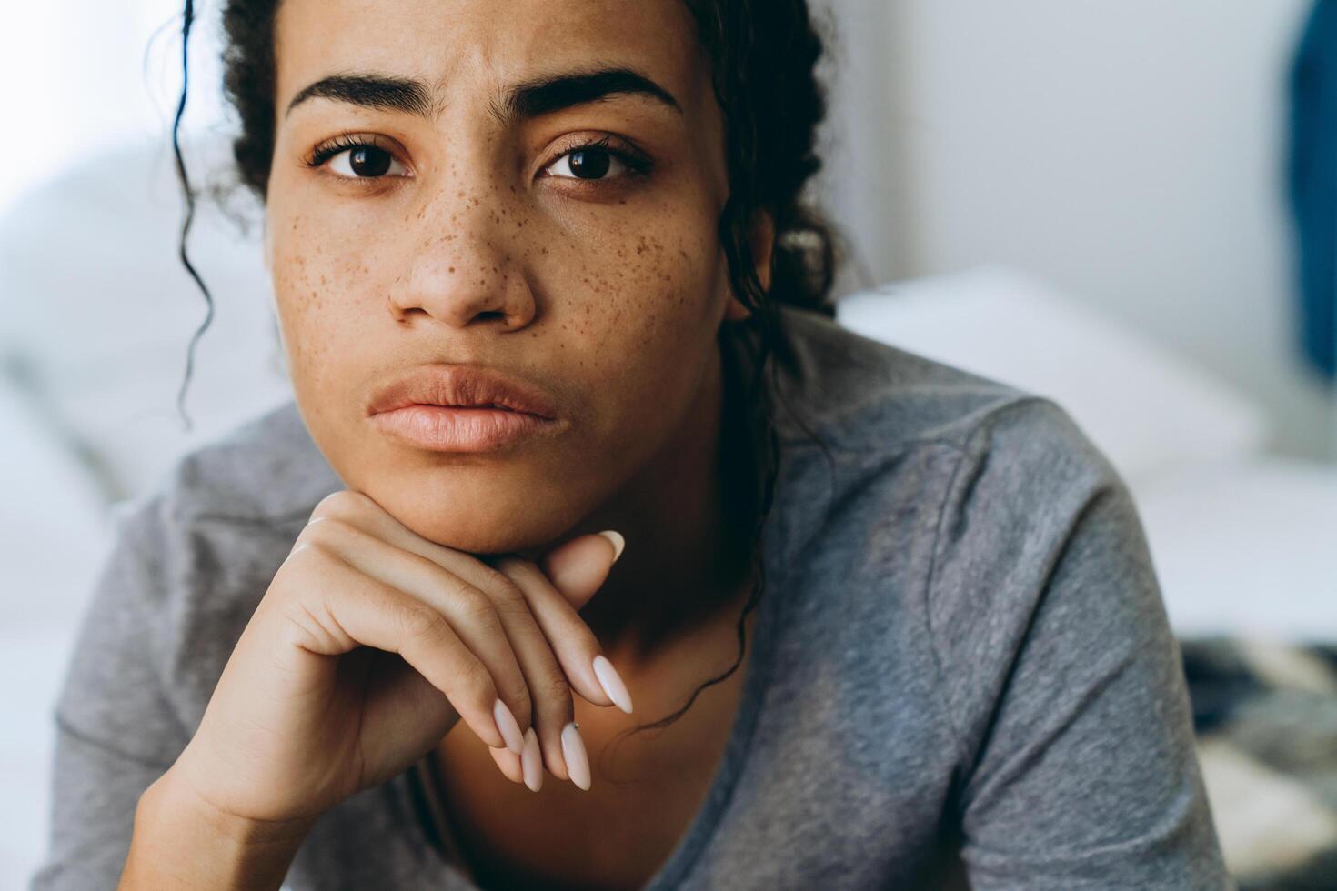 joven mujer negra con el ceño fruncido y mirando a la cámara en el dormitorio foto