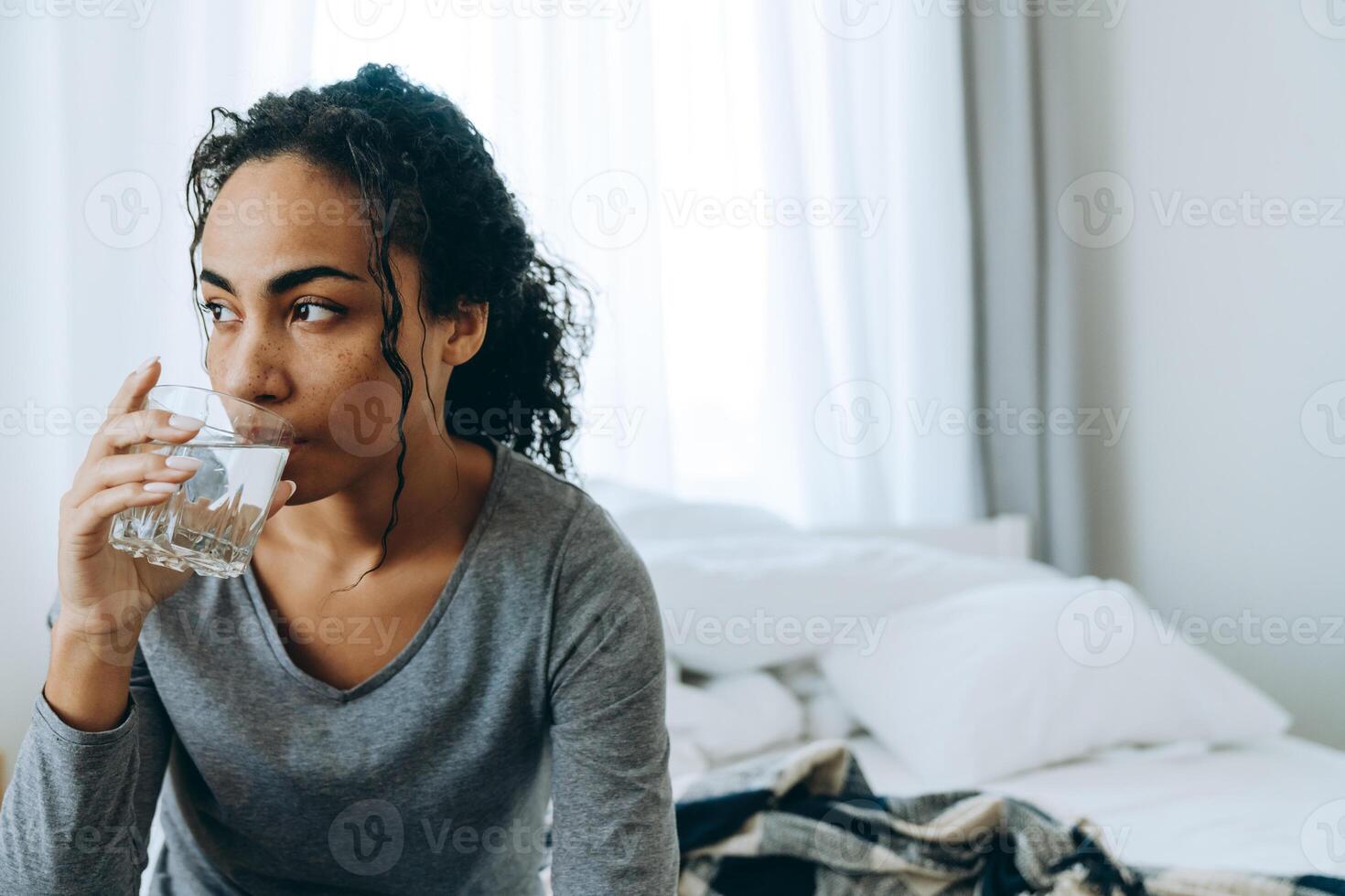 Black woman drinking water while sitting on bed at home photo