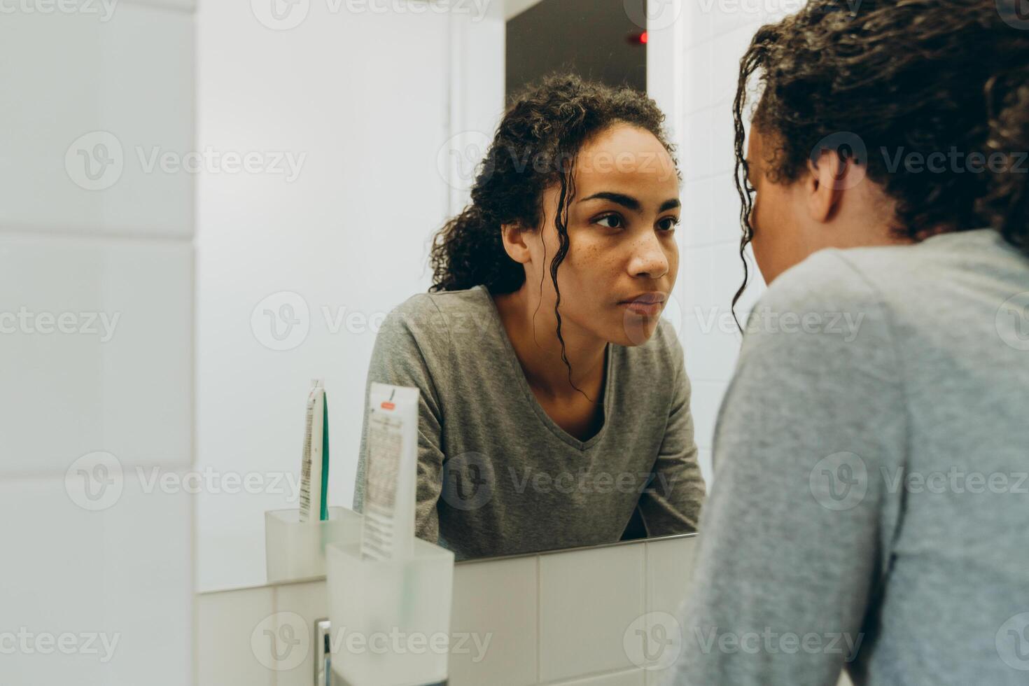 Black woman looking in mirror while standing in her bathroom photo