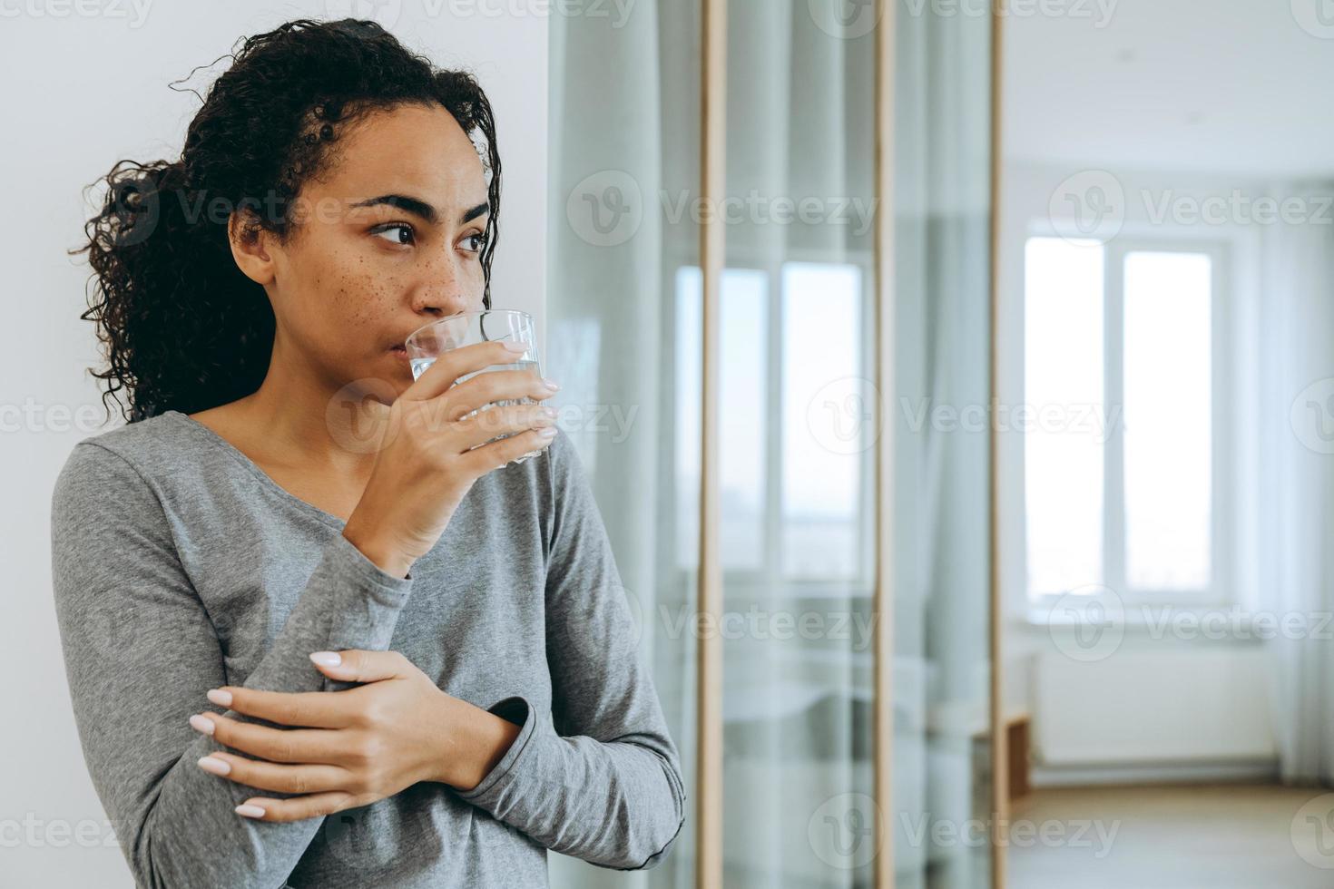 Young black woman drinking water during spending time at home photo