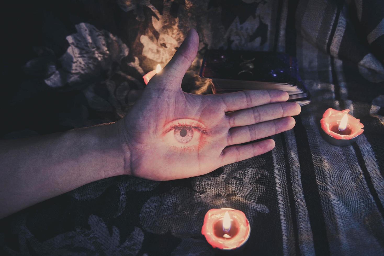 Mano con el ojo en busca de astrología, magia oculta, ilustración y velas encendidas a la luz de las velas en el fondo de la oscuridad - horóscopos espirituales mágicos y concepto de adivino de lectura de la palma de la mano foto