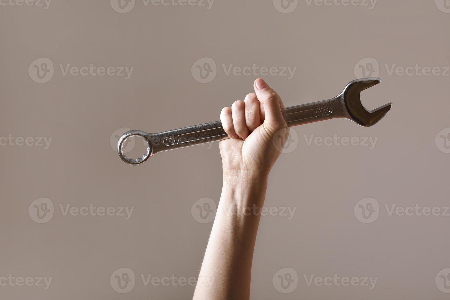 llave grande en la mano de la mujer. mano sostiene una llave sobre un fondo gris. llave combinada. llave grande de cromo vanadio en la mano. trabajo de mujeres. Día laboral. foto