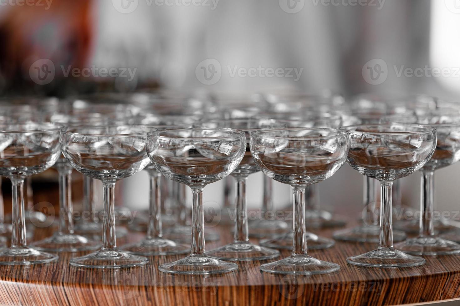 muchas elegantes copas vacías de vino o champán en la mesa de madera en el día de la boda. conjunto de vasos vacíos en blanco que se muestran en filas. preparación para las vacaciones foto