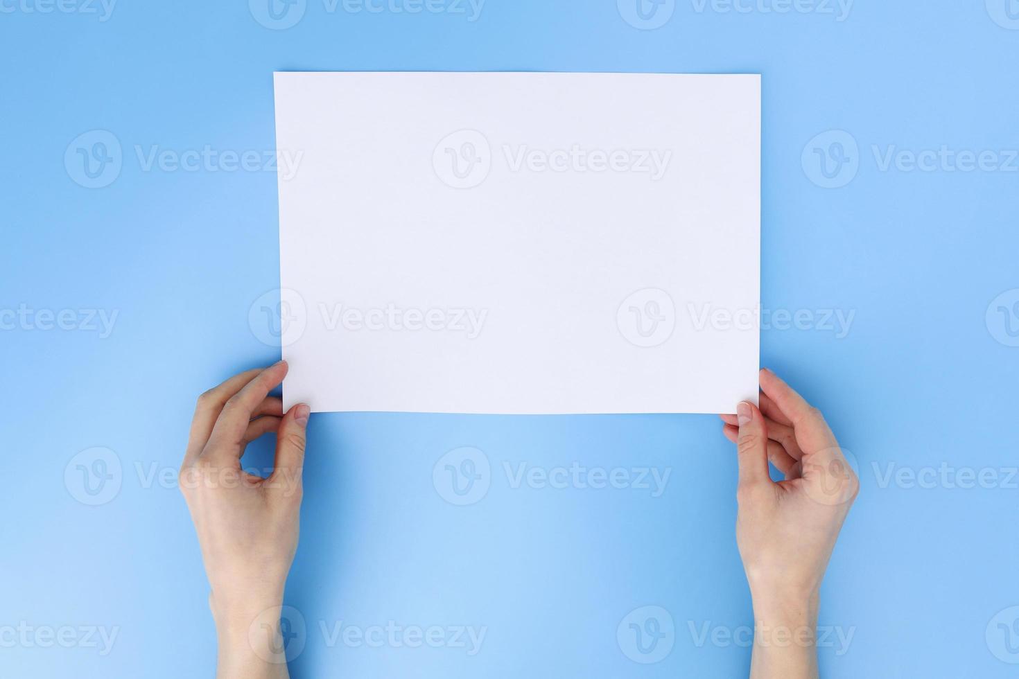 Woman hand holding the paper on blue background. place for text. blank piece of inscription paper photo
