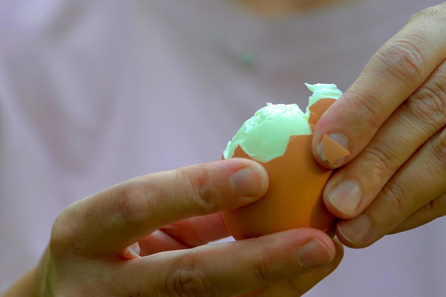Las manos de las mujeres limpian el huevo de gallina hervido de la cáscara. foto