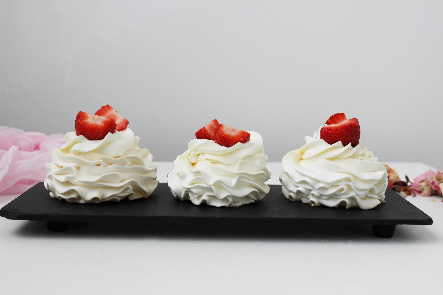 Cupcakes with white cream and strawberries on a black plate. Horizontal photo. photo