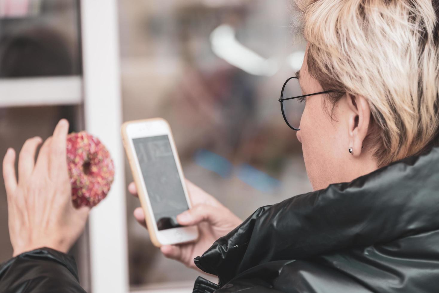 a girl with short hair and glasses is sitting in a cafe and photographing a sweet donut on her phone portrait in warm colors photo