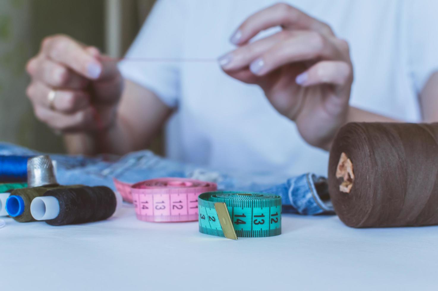 women's hands, a tailor sews clothes at a table on which spools of thread lie photo