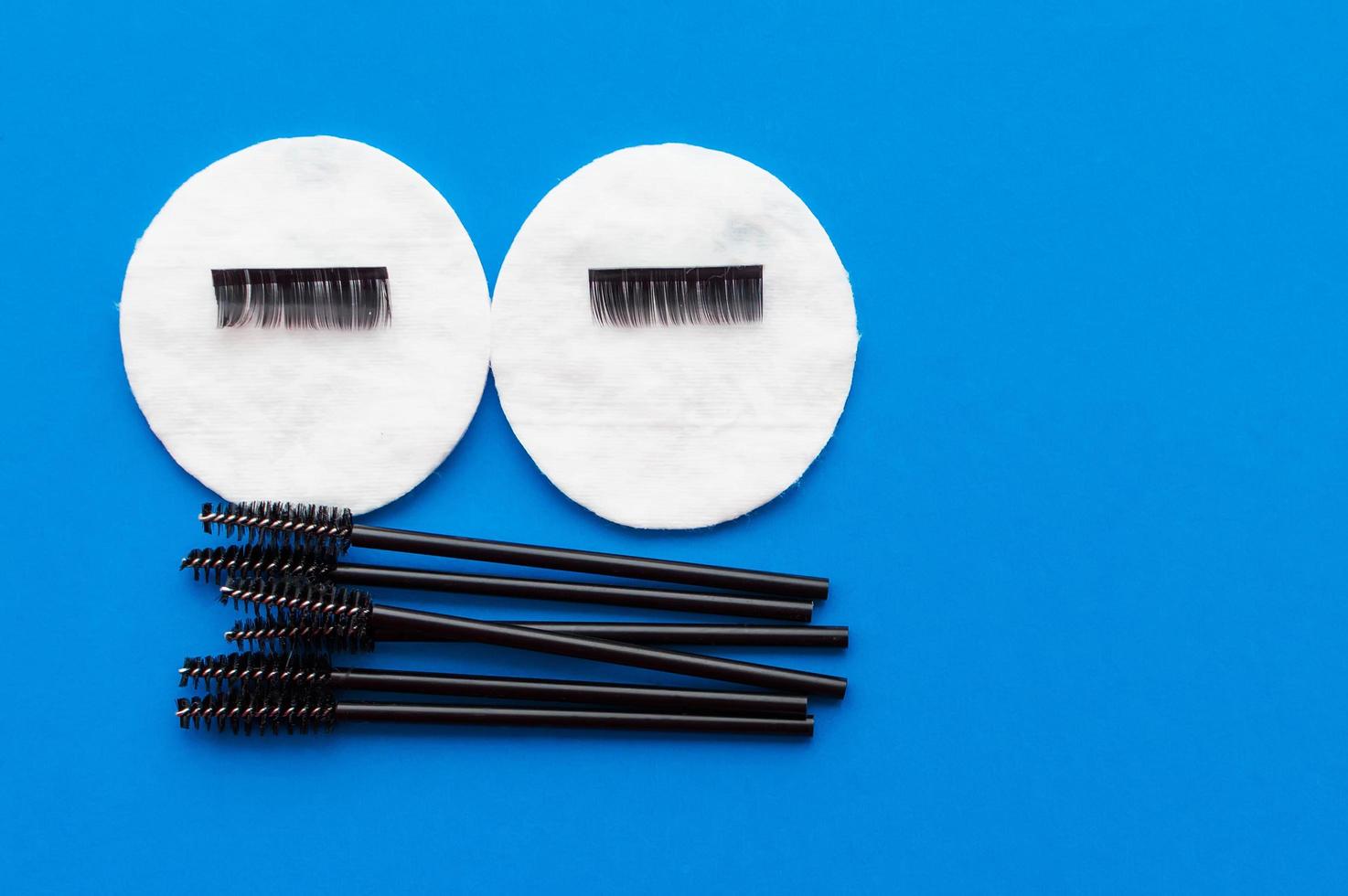 The concept of eyelash extension. Brushes and artificial eyelashes on cotton pads on a blue background with a place for writing. photo