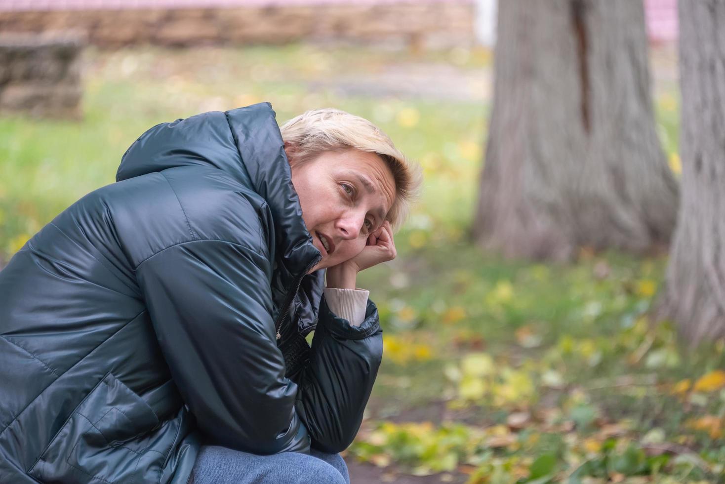 a girl in a dark jacket sits on a bench against the background of autumn thinking photo