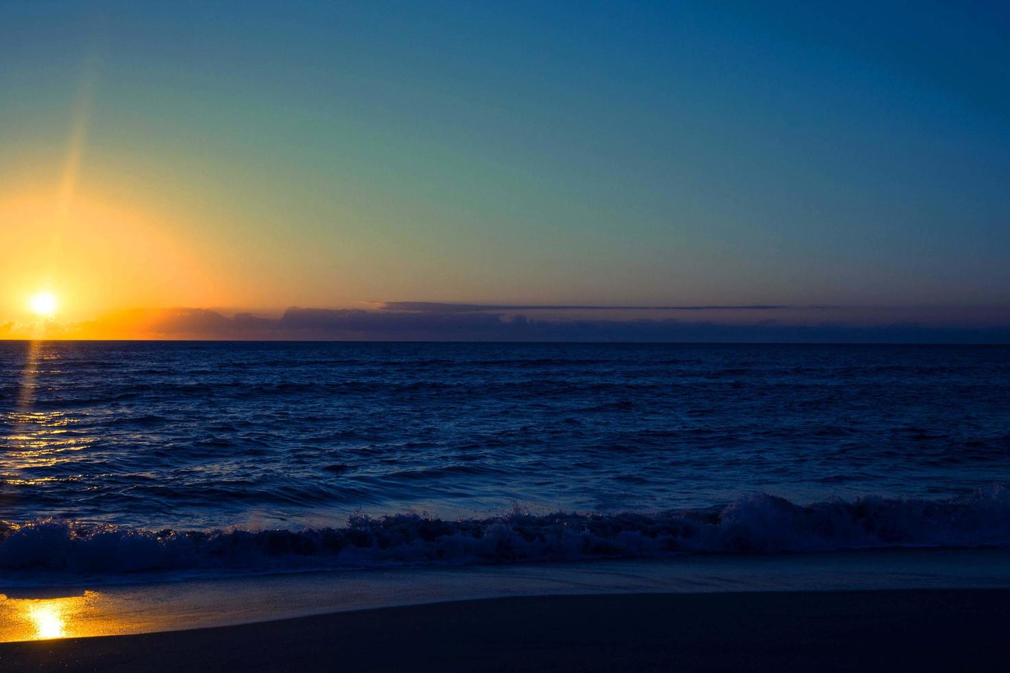 puesta de sol naranja en el mar y el cielo azul hermoso mar y puesta de sol con gran sol amarillo bajo las colinas de la superficie del mar en el fondo. foto