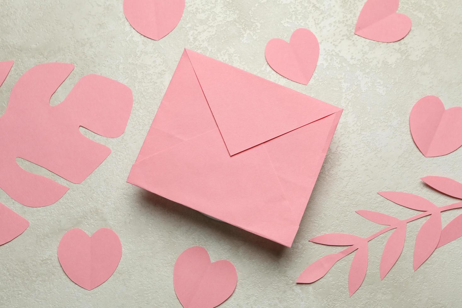 Envelope, paper leaves and hearts on white textured background photo
