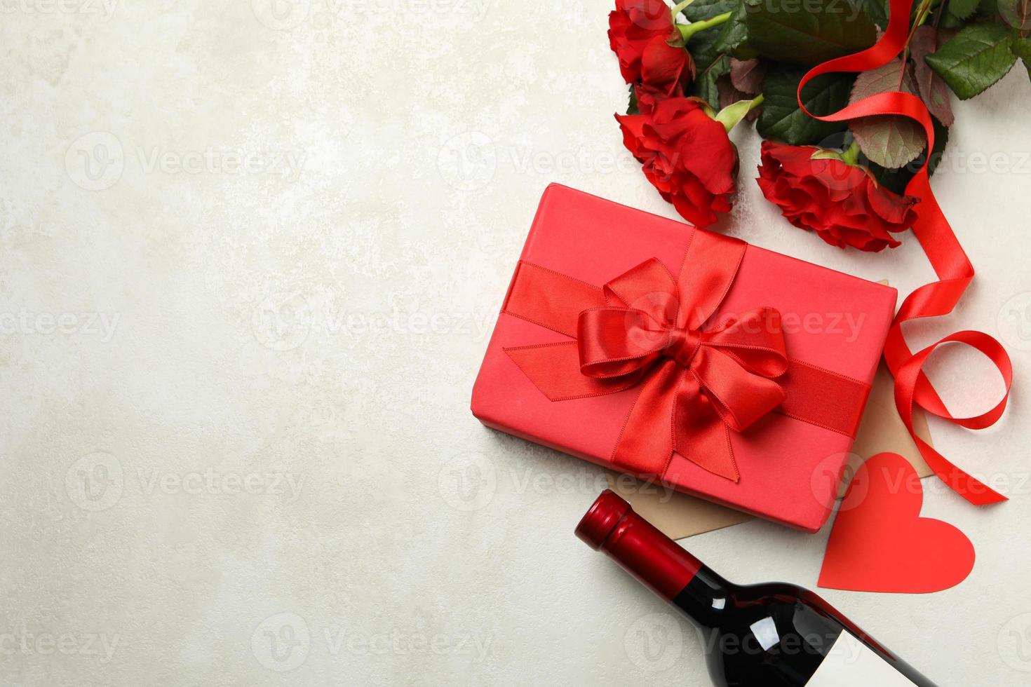 Concept of Valentine's day with roses, wine and gift box on white textured background photo