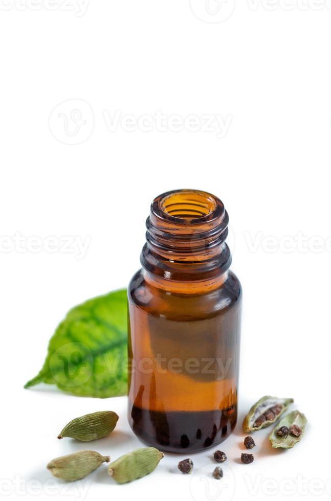 una botella de aceite esencial de cardamomo con semillas de cardamomo y hojas en blanco foto
