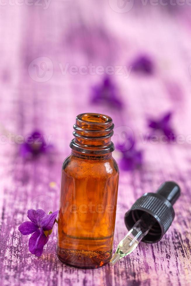 Aceite y flor de violetas, piedras zen sobre fondo de madera púrpura foto