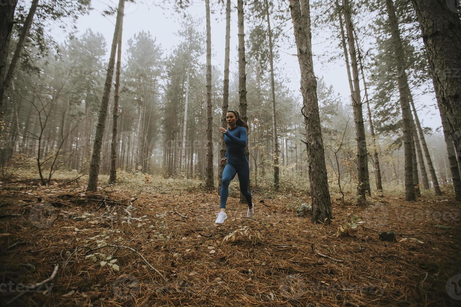 Young woman running toward camera on the forest trail at autumn photo