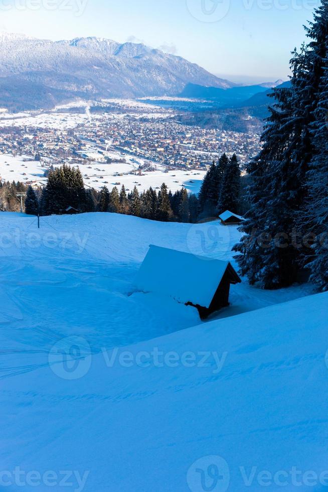 Cottage in snow covered mountain side with view over Garmisch Partenkirchen photo