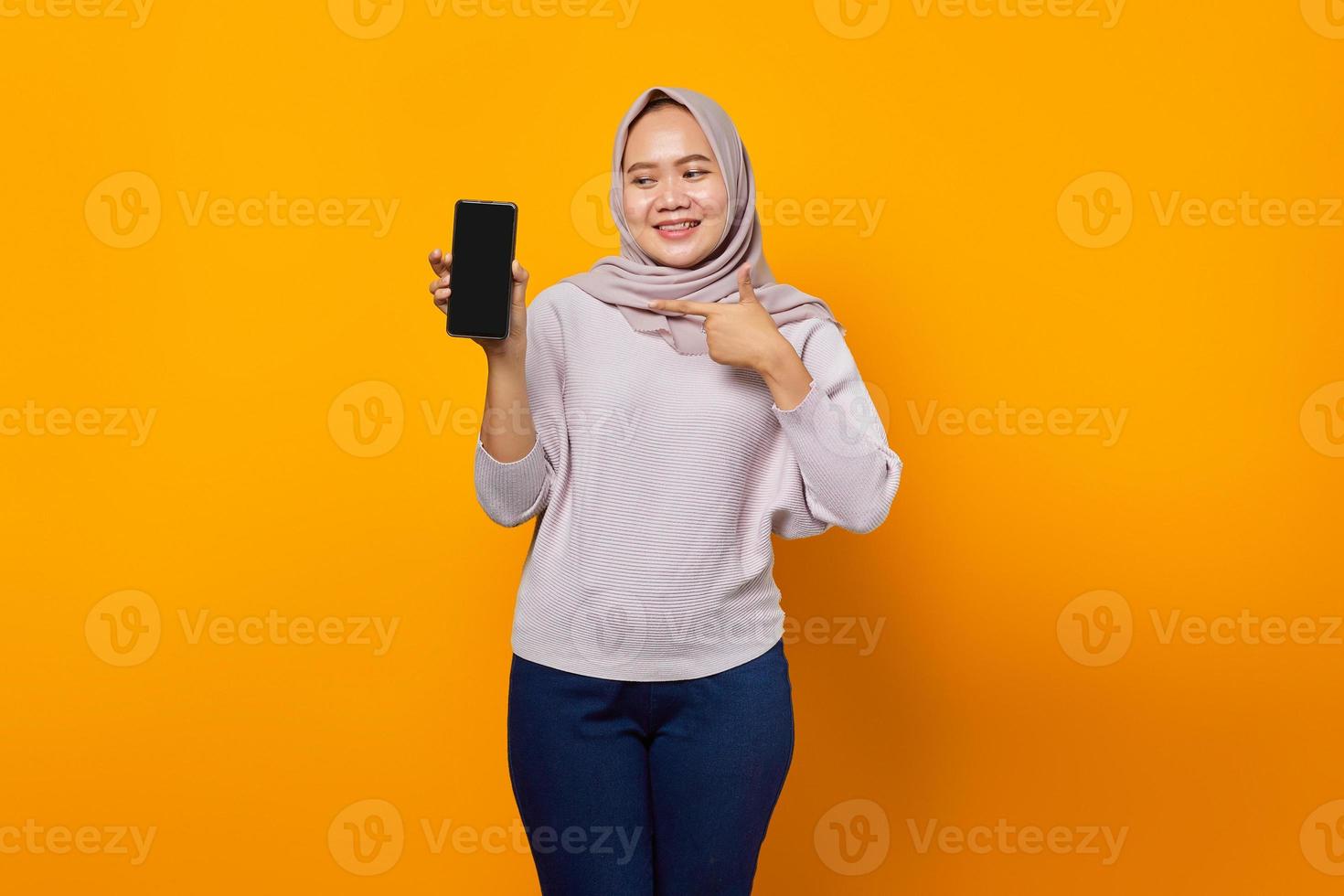 Alegre joven asiática mostrando la pantalla en blanco del smartphone aislado sobre fondo amarillo foto