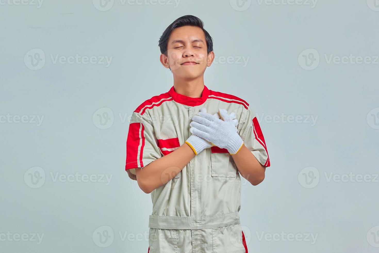Portrait of handsome man wearing mechanic uniform with both palms on chest on gray background photo