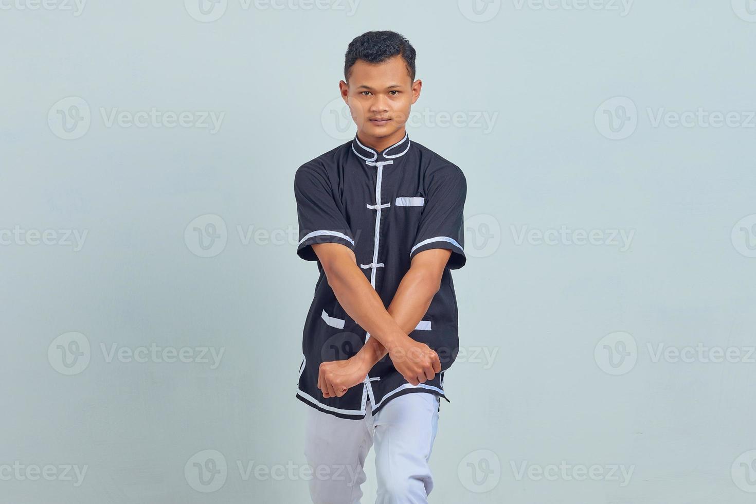 Portrait of Asian young man wearing taekwondo kimono showing boxer gesture over gray background photo